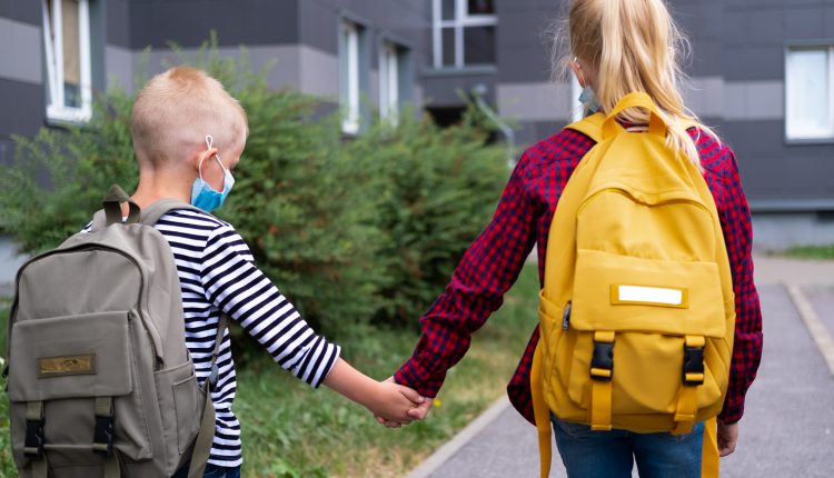 back view Brother and sister going school after pandemic over. Kids wearing mask and backpacks protect and safety from coronavirus for back to school. students are ready for new school year