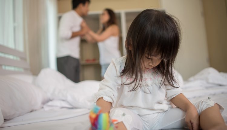 Little Girl sitting with her parents on the bed looking serious