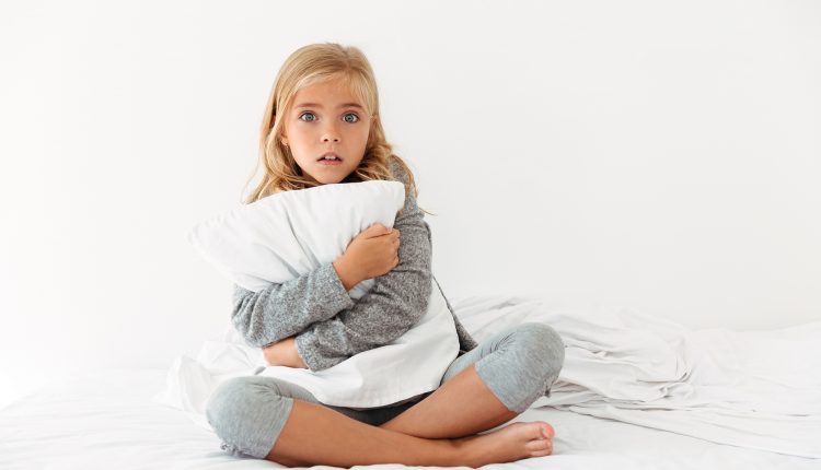 Portrait of a scared little girl hugging pillow