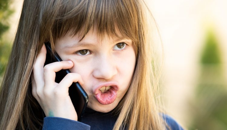 Portrait of angry child girl with long hair talking on cell phon