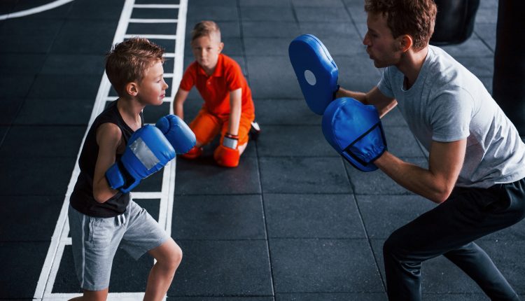 Young trainer teaches kids boxing sport in the gym