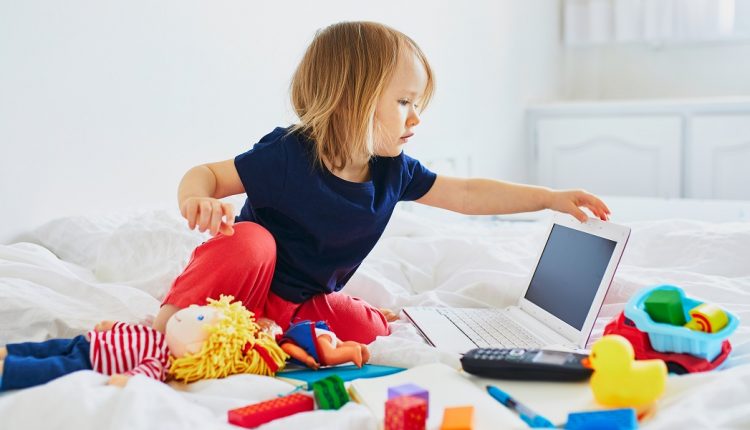 Toddler girl with laptop, notebook, phone and different toys in bed