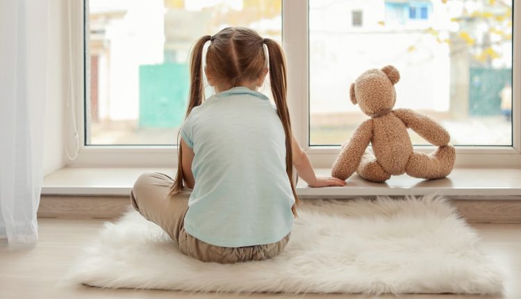 Lonely little girl with teddy bear sitting near window. Autism c